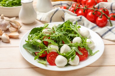 Photo of Tasty salad with arugula, spinach, mozzarella cheese and tomatoes on wooden table, closeup