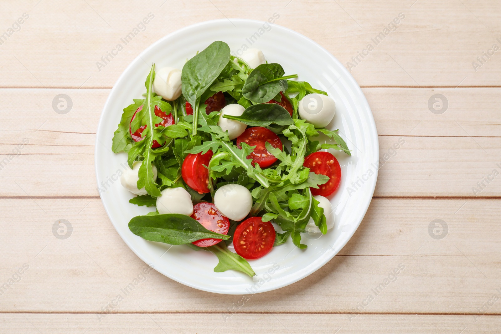 Photo of Tasty salad with arugula, spinach, mozzarella cheese and tomatoes on wooden table, top view