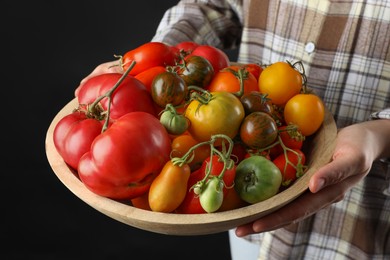 Woman holding bowl of different fresh tomatoes on black background, closeup