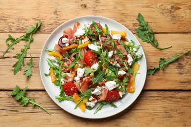 Photo of Tasty salad with arugula, cheese and vegetables on wooden table, flat lay