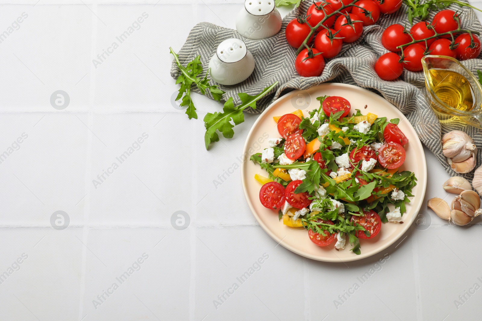 Photo of Tasty salad with arugula, cheese and vegetables on white tiled table, flat lay. Space for text