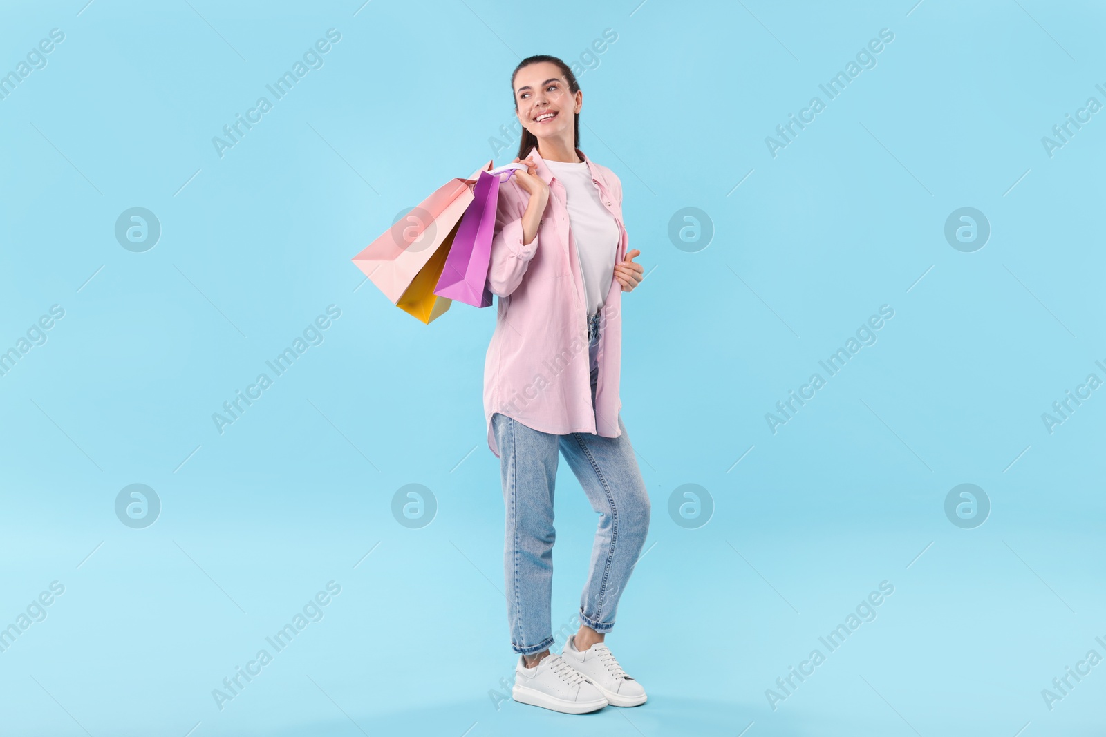 Photo of Smiling woman with colorful shopping bags on light blue background