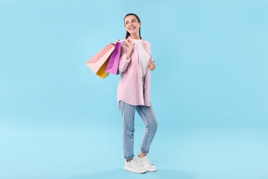 Smiling woman with colorful shopping bags on light blue background