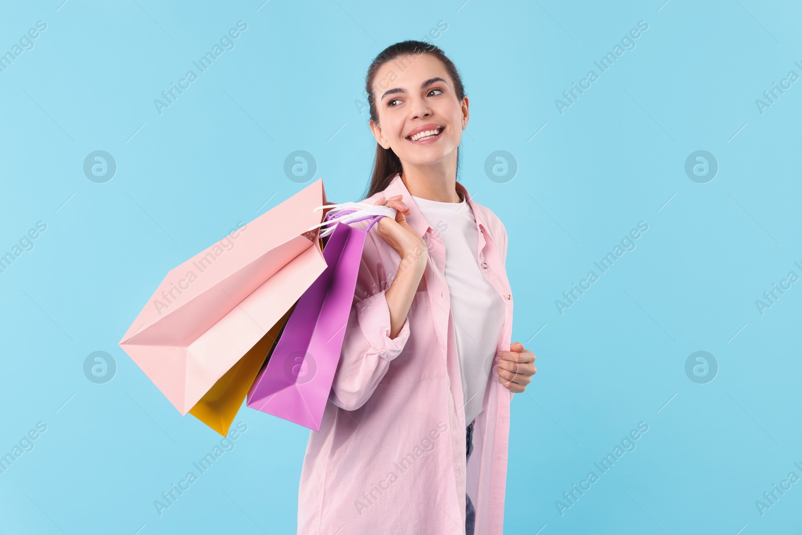 Photo of Smiling woman with colorful shopping bags on light blue background