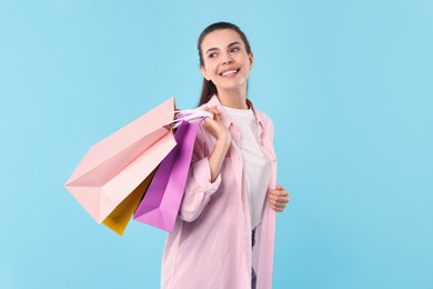 Smiling woman with colorful shopping bags on light blue background