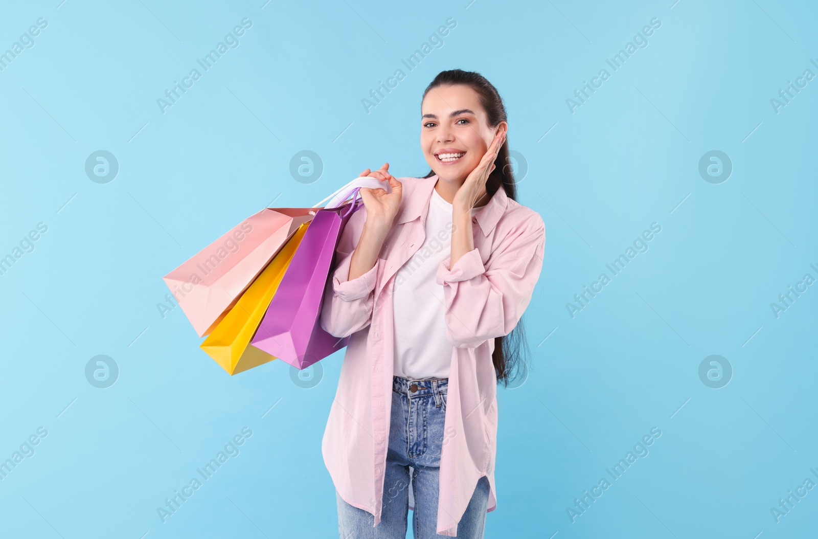 Photo of Smiling woman with colorful shopping bags on light blue background