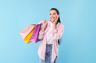 Photo of Smiling woman with colorful shopping bags on light blue background