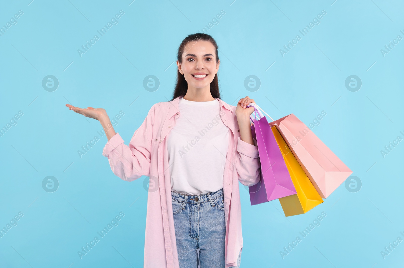 Photo of Smiling woman with colorful shopping bags holding something on light blue background