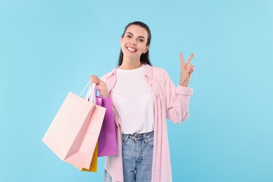 Photo of Smiling woman with colorful shopping bags showing peace sign on light blue background