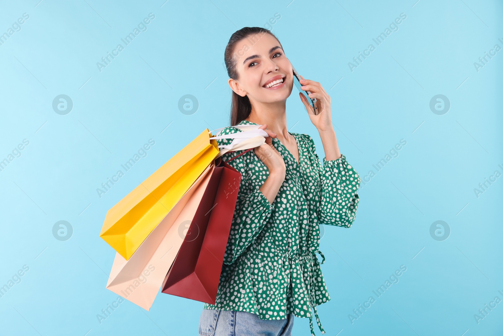 Photo of Smiling woman with shopping bags talking on smartphone against light blue background