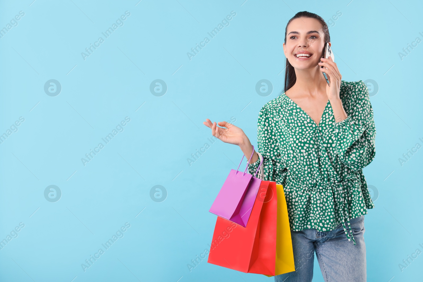 Photo of Smiling woman with shopping bags talking on smartphone against light blue background. Space for text