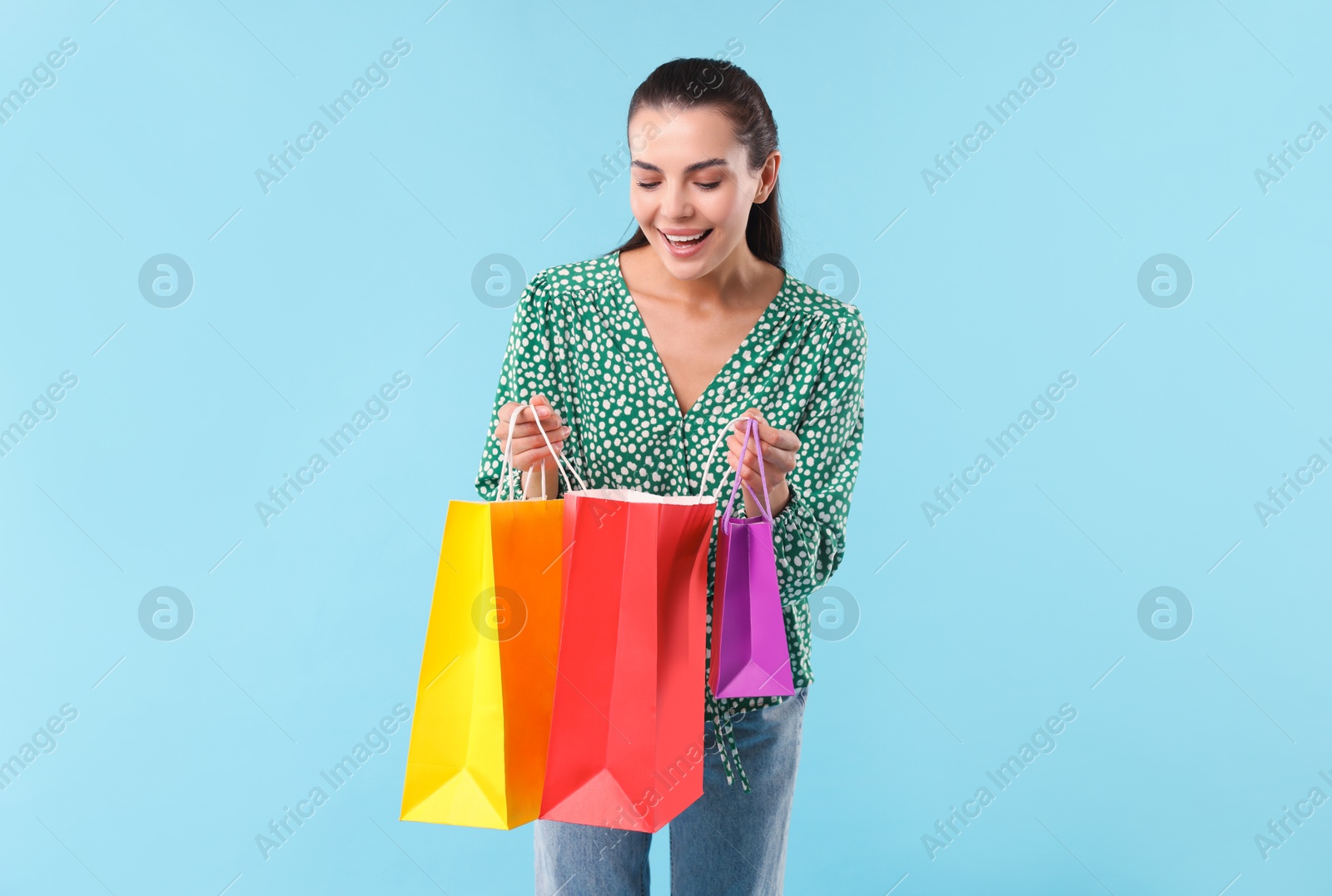 Photo of Happy woman looking into shopping bag on light blue background