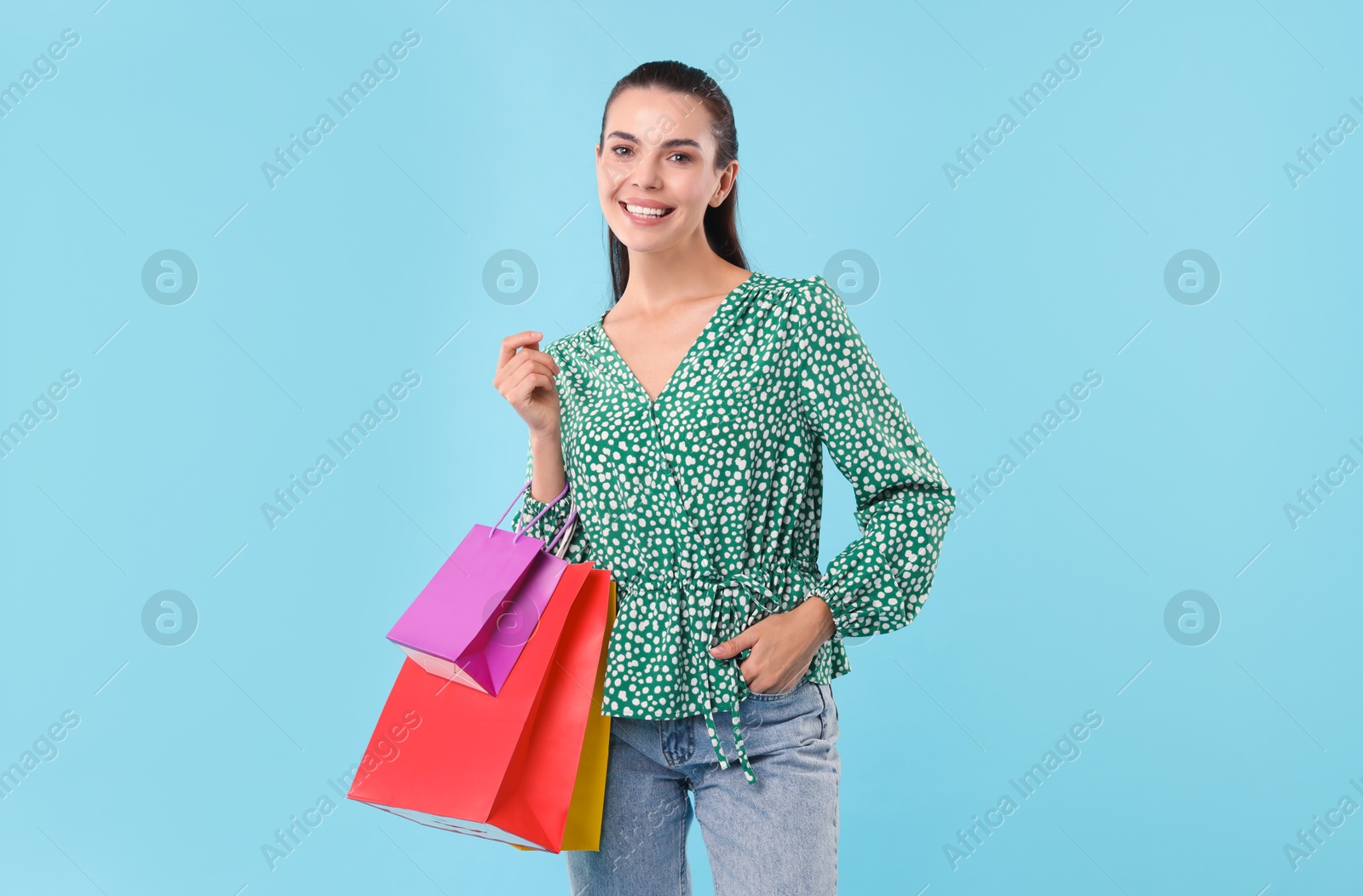 Photo of Smiling woman with colorful shopping bags on light blue background