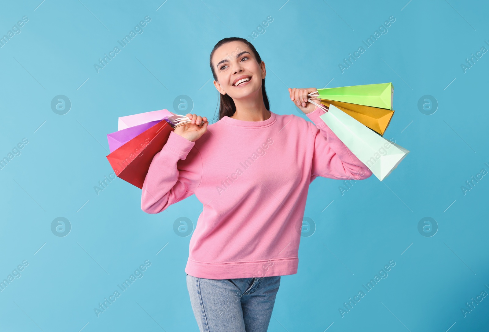 Photo of Happy woman with shopping bags on light blue background. Space for text