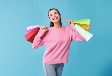 Photo of Happy woman with shopping bags on light blue background. Space for text