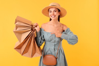 Smiling woman pointing at shopping bags on yellow background