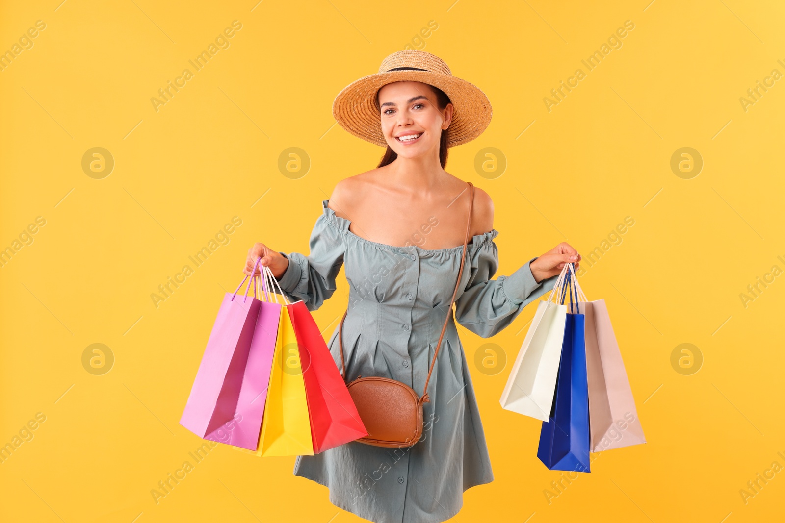 Photo of Smiling woman with colorful shopping bags on yellow background