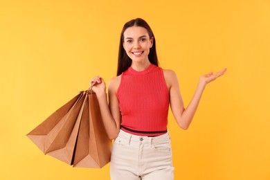 Photo of Smiling woman with shopping bags holding something on yellow background