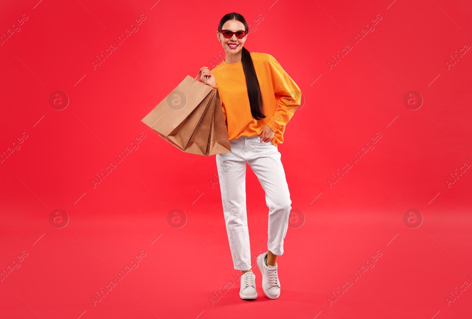 Photo of Smiling woman with shopping bags on red background