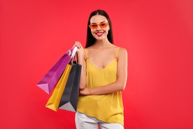 Photo of Smiling woman with colorful shopping bags on red background