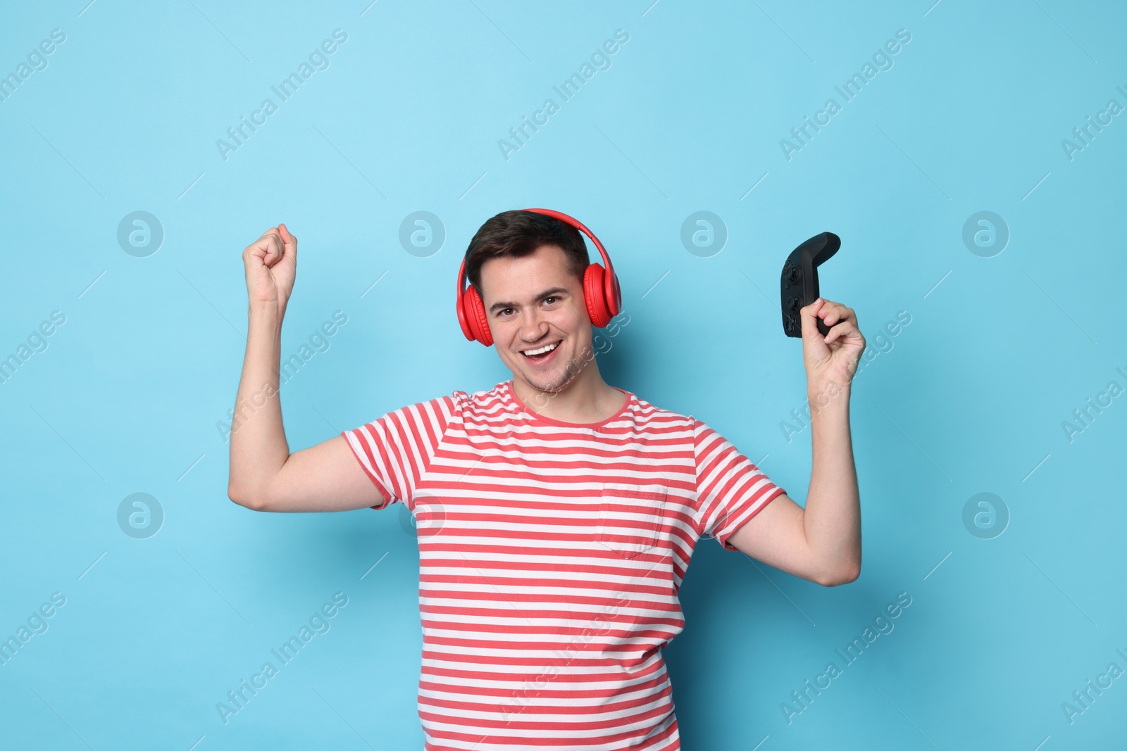 Photo of Happy young man in headphones with controller on light blue background