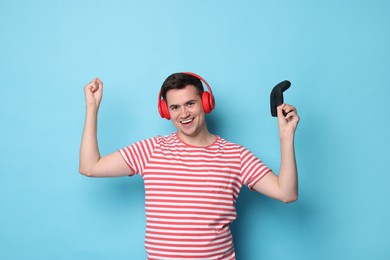 Photo of Happy young man in headphones with controller on light blue background