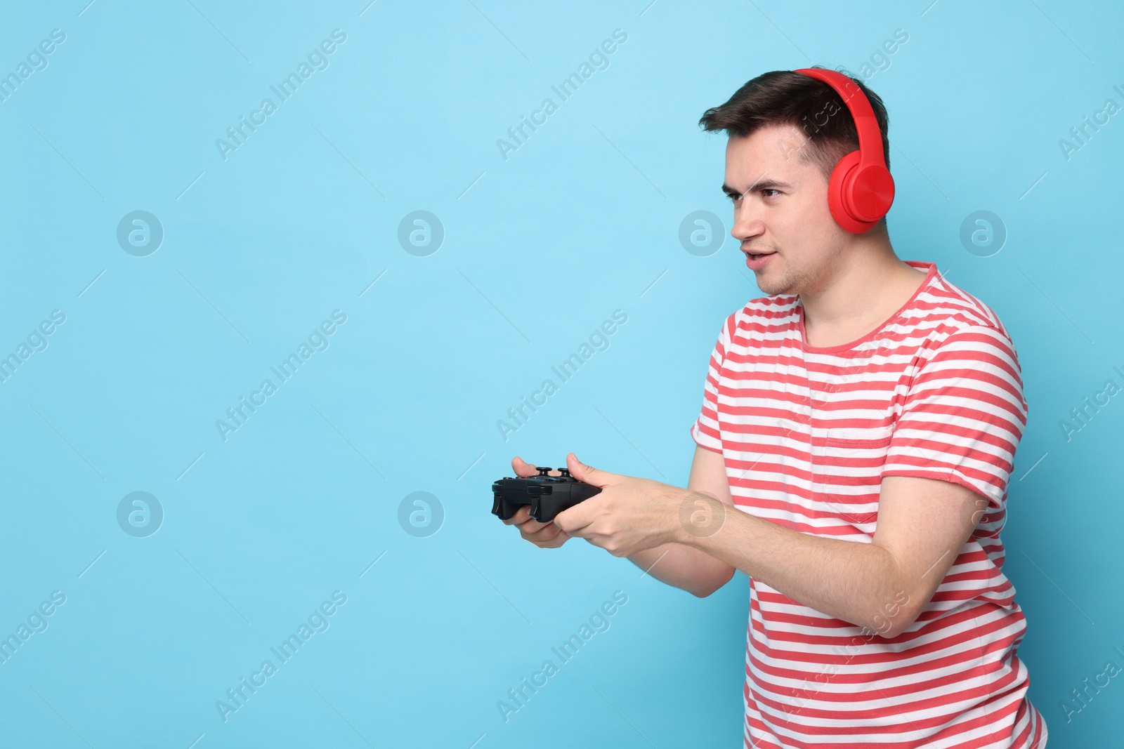 Photo of Young man in headphones playing video games with controller on light blue background, space for text