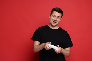 Happy young man playing video games with controller on red background