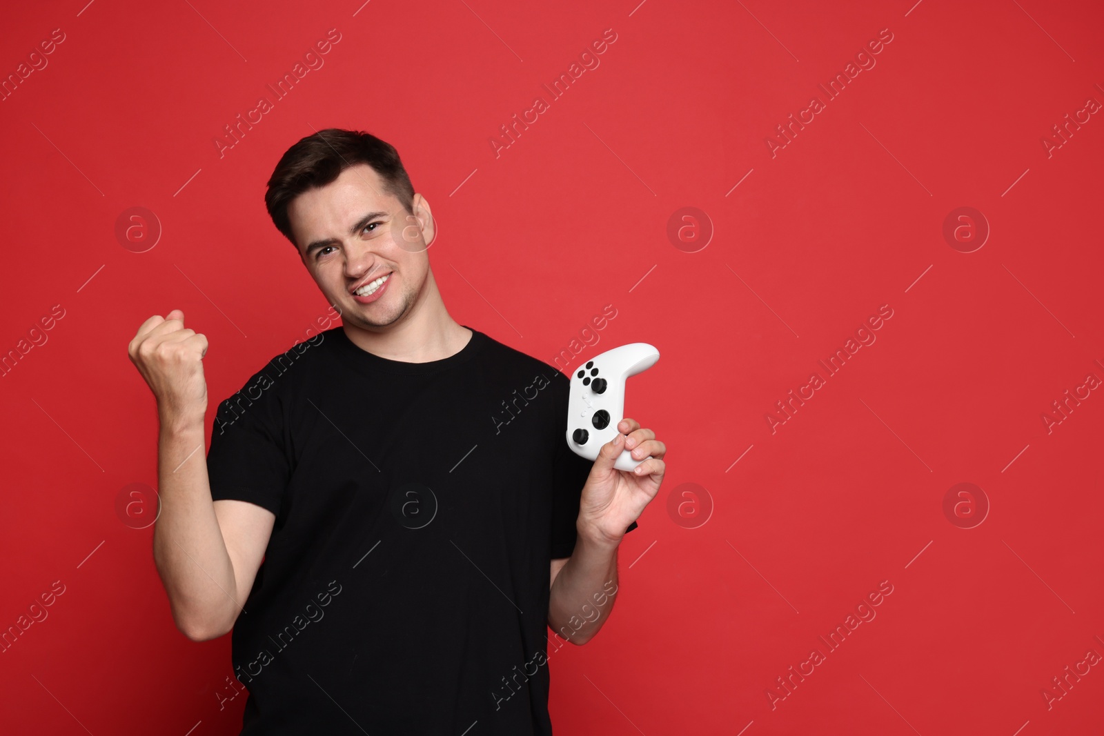 Photo of Happy young man with controller on red background, space for text