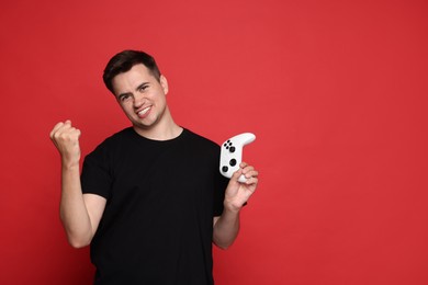 Happy young man with controller on red background, space for text