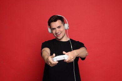 Happy young man in headphones playing video games with controller on red background