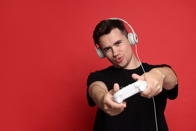 Young man in headphones playing video games with controller on red background, space for text