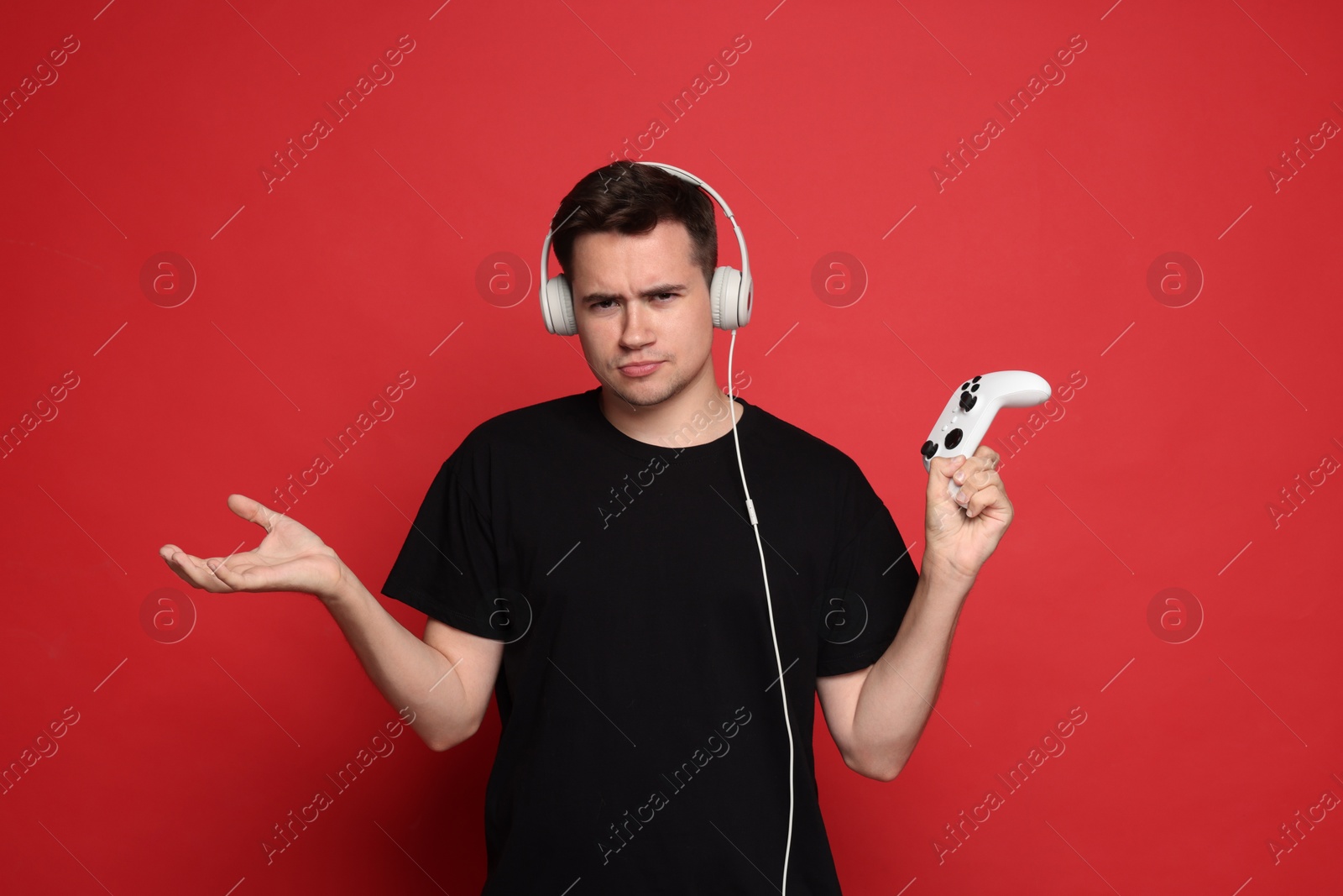 Photo of Young man in headphones with controller on red background