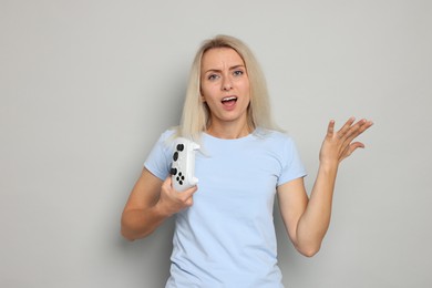 Unhappy woman with controller on gray background