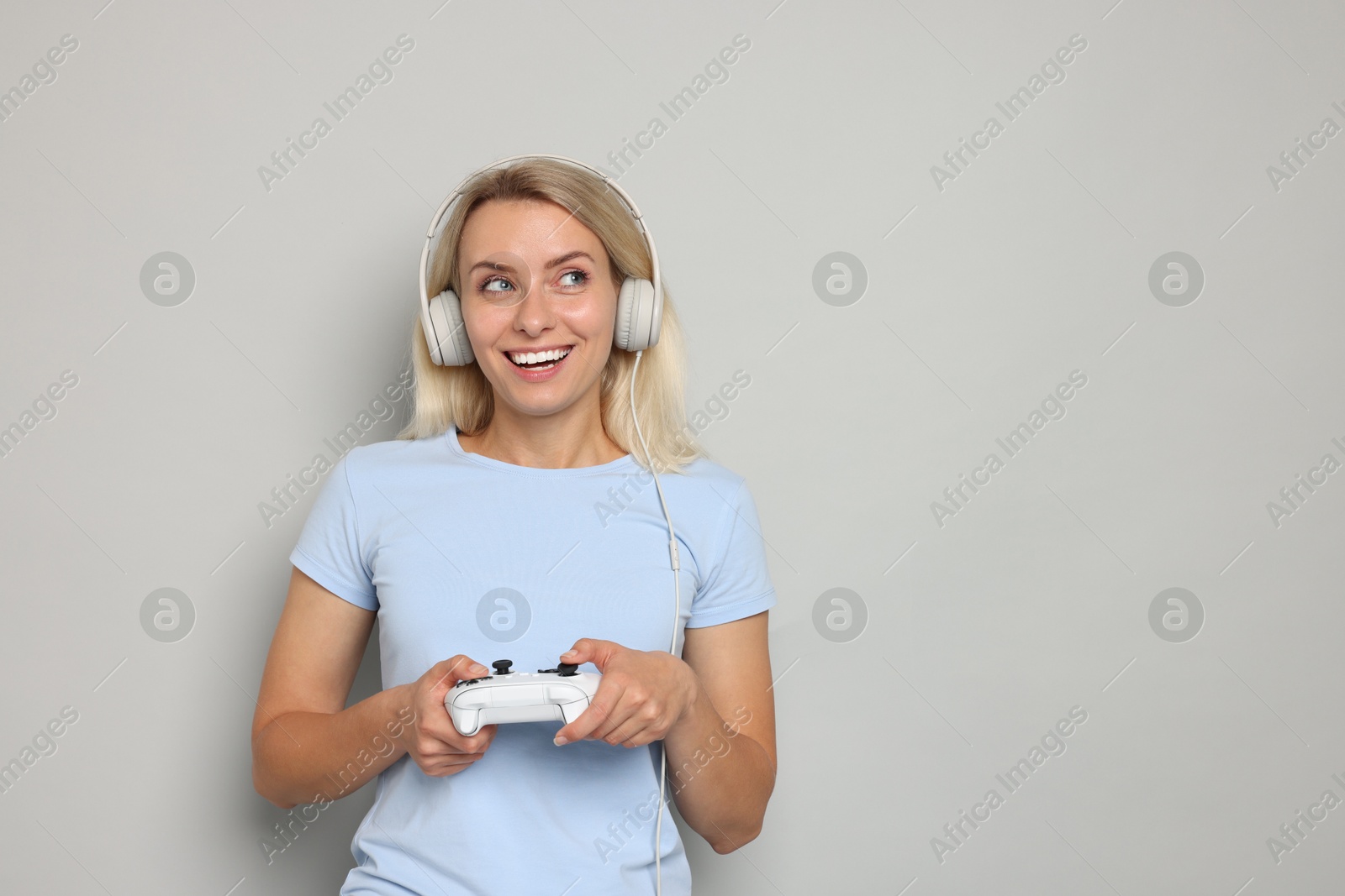 Photo of Happy woman in headphones playing video games with controller on gray background, space for text