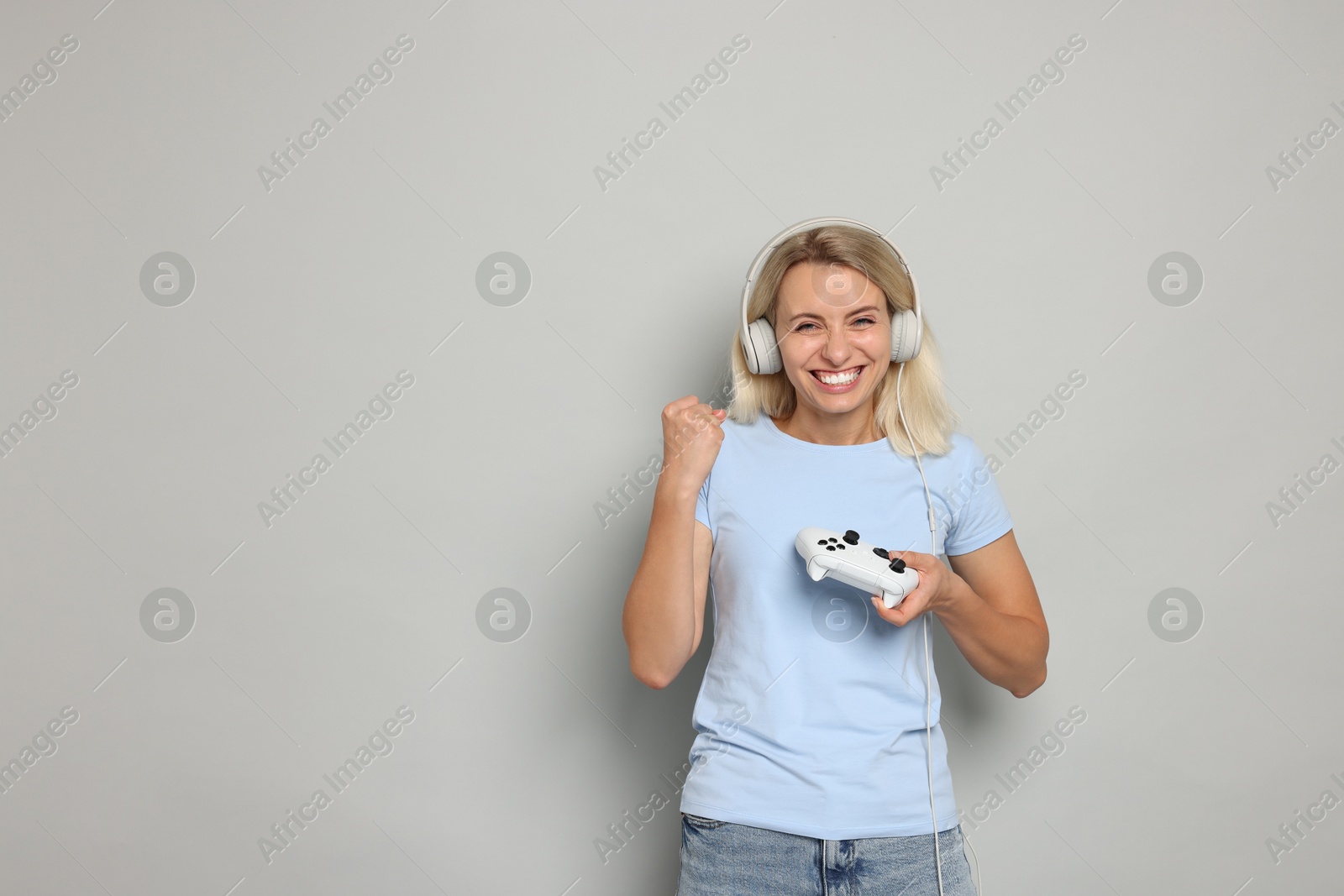 Photo of Happy woman in headphones with controller on gray background, space for text