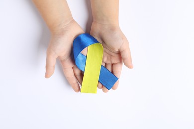 Photo of Child with yellow and blue ribbon on white background, top view. Down syndrome awareness