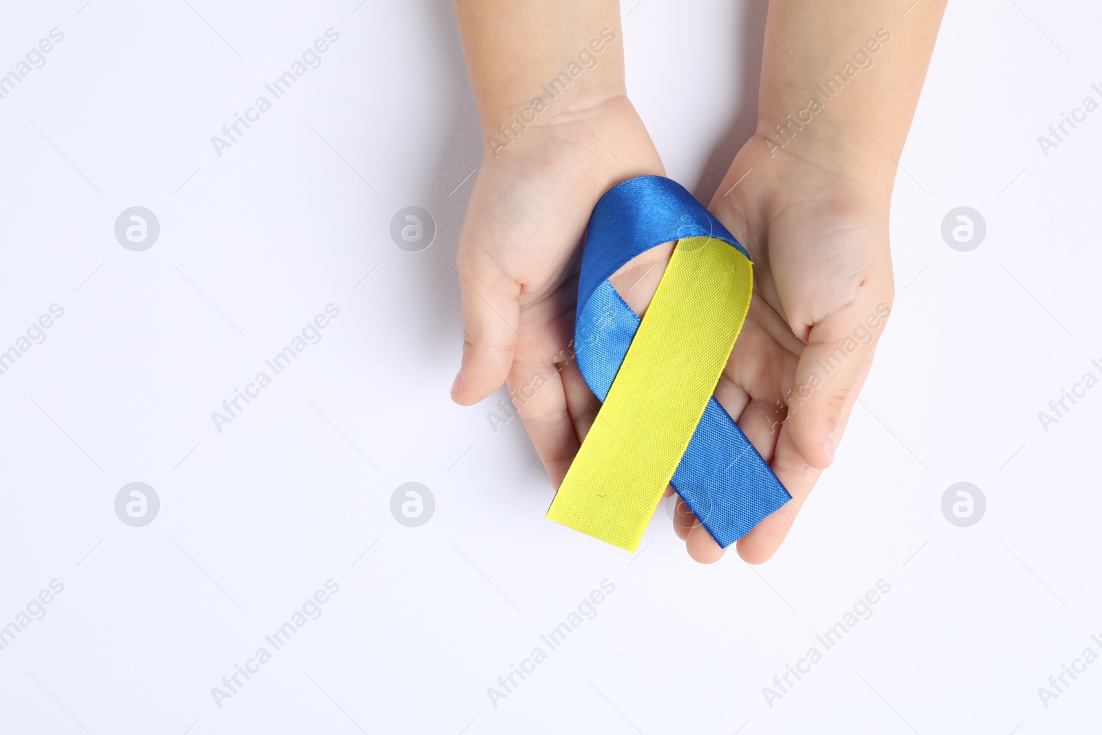 Photo of Child with yellow and blue ribbon on white background, top view. Down syndrome awareness