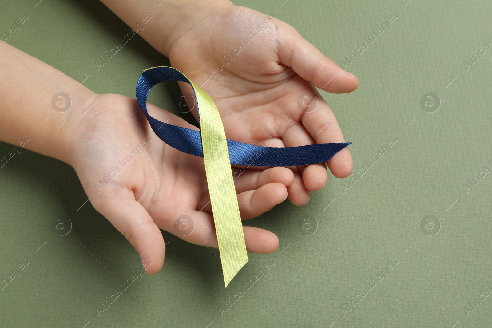 Photo of Child with yellow and blue ribbon on green background, closeup. Down syndrome awareness