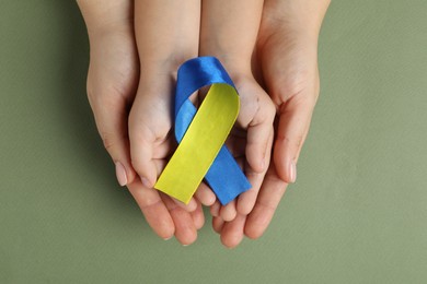 Photo of Woman with child holding yellow and blue ribbon on green background, top view. Down syndrome awareness