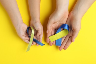 Photo of Woman with child holding yellow and blue ribbons on color background, top view. Down syndrome awareness