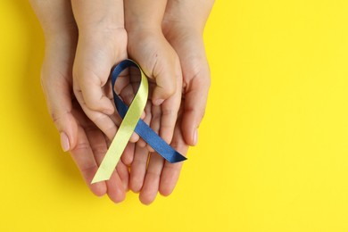 Photo of Woman with child holding yellow and blue ribbon on color background, top view. Down syndrome awareness