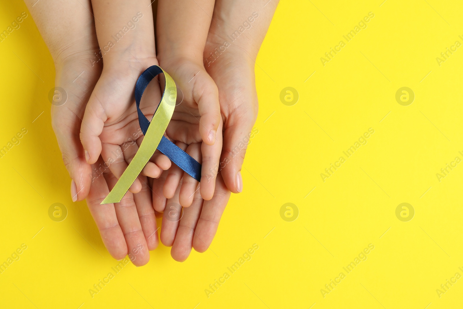 Photo of Woman with child holding yellow and blue ribbon on color background, top view. Down syndrome awareness