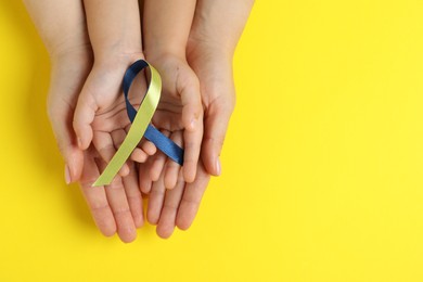 Photo of Woman with child holding yellow and blue ribbon on color background, top view. Down syndrome awareness