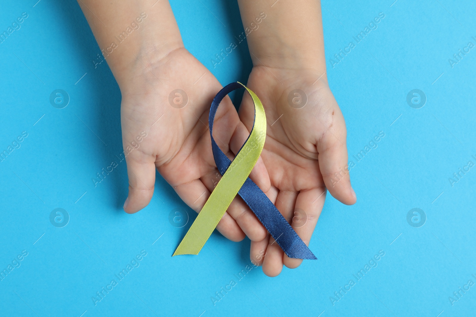 Photo of Child with yellow and blue ribbon on color background, top view. Down syndrome awareness