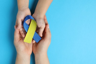 Photo of Woman with child holding yellow and blue ribbons on color background, top view. Down syndrome awareness