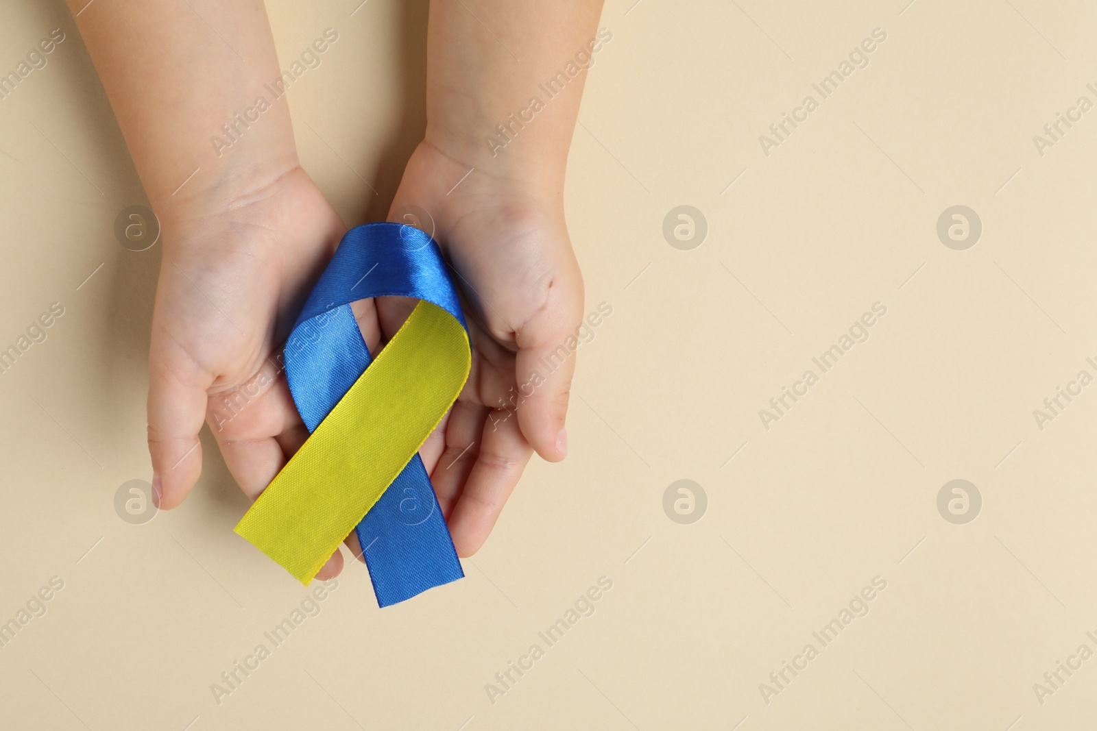 Photo of Child with yellow and blue ribbon on beige background, top view. Down syndrome awareness