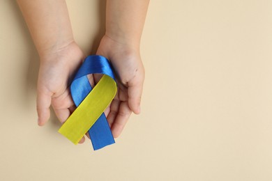 Photo of Child with yellow and blue ribbon on beige background, top view. Down syndrome awareness