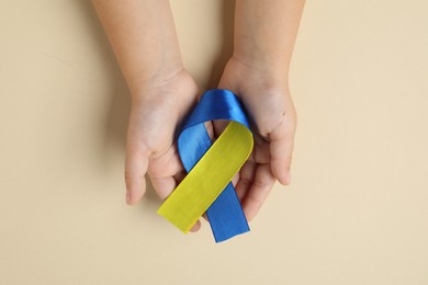 Photo of Child with yellow and blue ribbon on beige background, top view. Down syndrome awareness