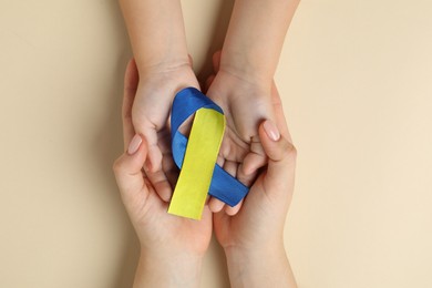 Photo of Woman with child holding yellow and blue ribbon on beige background, top view. Down syndrome awareness